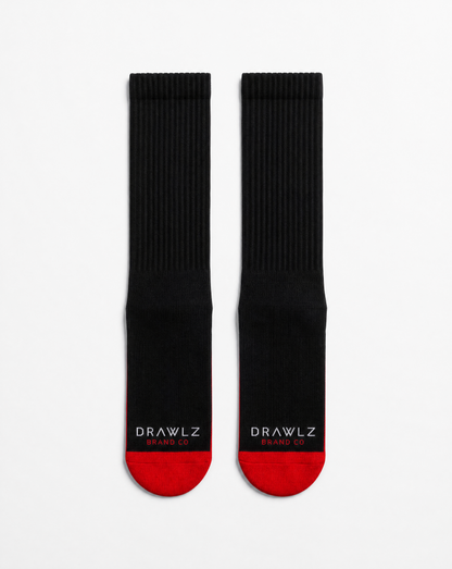 A pair of black crew socks with red toes and heels, featuring the white text 'DRAWLZ DESIGN CO.' printed on the soles, displayed against a clean white background.
