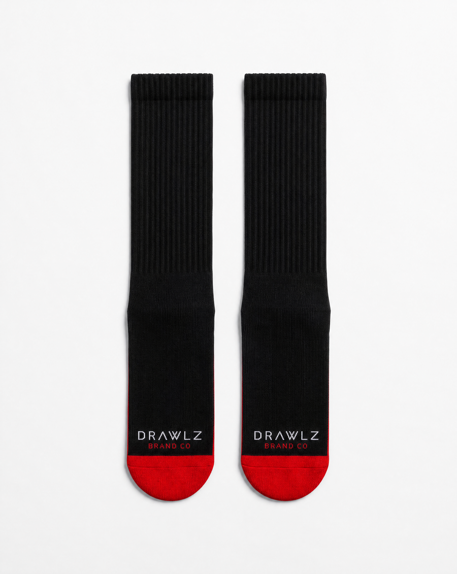 A pair of black crew socks with red toes and heels, featuring the white text 'DRAWLZ DESIGN CO.' printed on the soles, displayed against a clean white background.